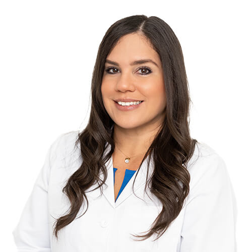 A professional headshot of Dr. Kriselle Torres, M.D. She has long brown hair and is wearing a white lab coat over a turquoise blue shirt.