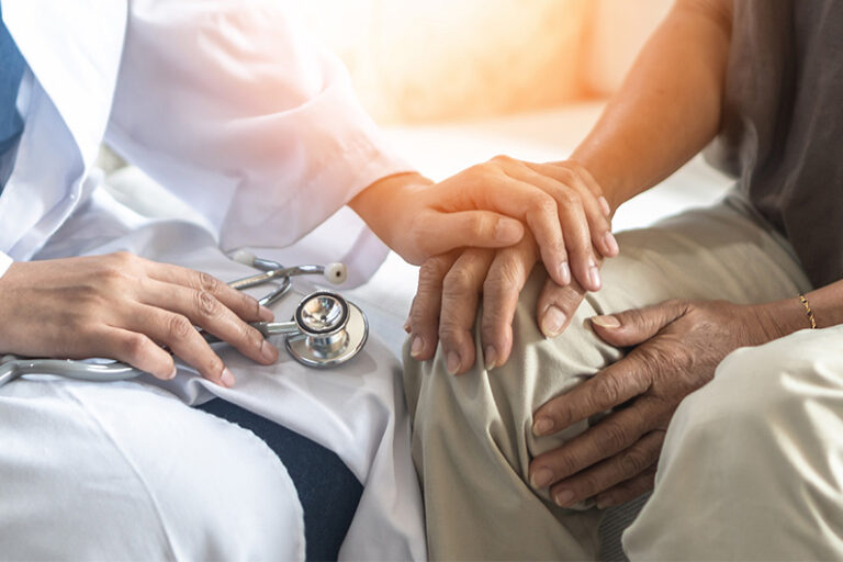 A doctor comforts a patient by putting his hand on the patient's.