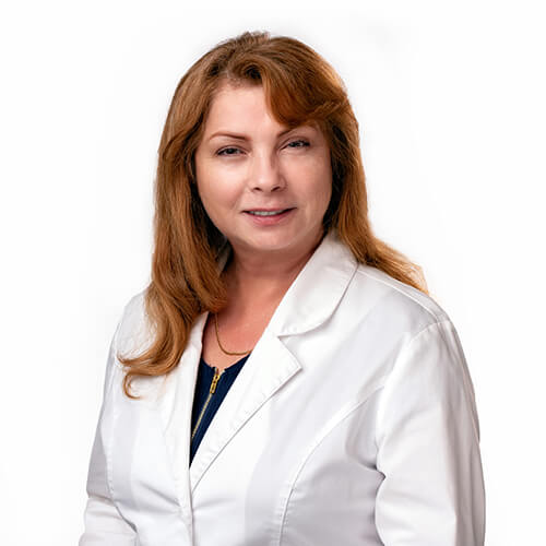 A headshot of Rose Zapata, APRN, wearing a white lab coat. She is a caucasian female with red hair