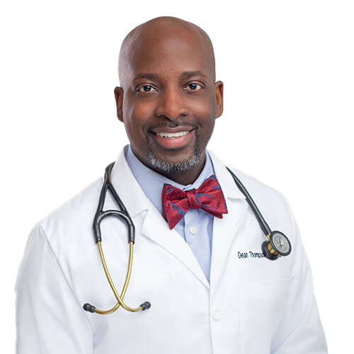 A headshot of Dr. Dean Thompson. He is wearing a light blue shirt with a red and blue bowtie, along with a white lab coat and stethoscope.